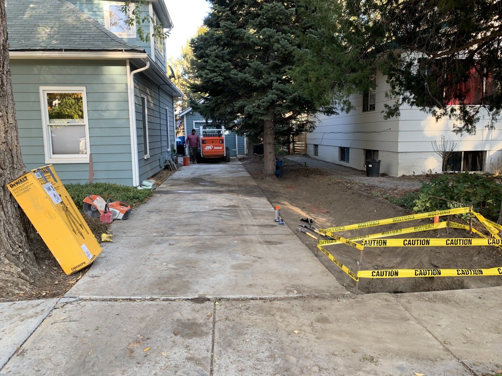 Concrete driveway under construction; building and trees on either side; caution tape and tools present.