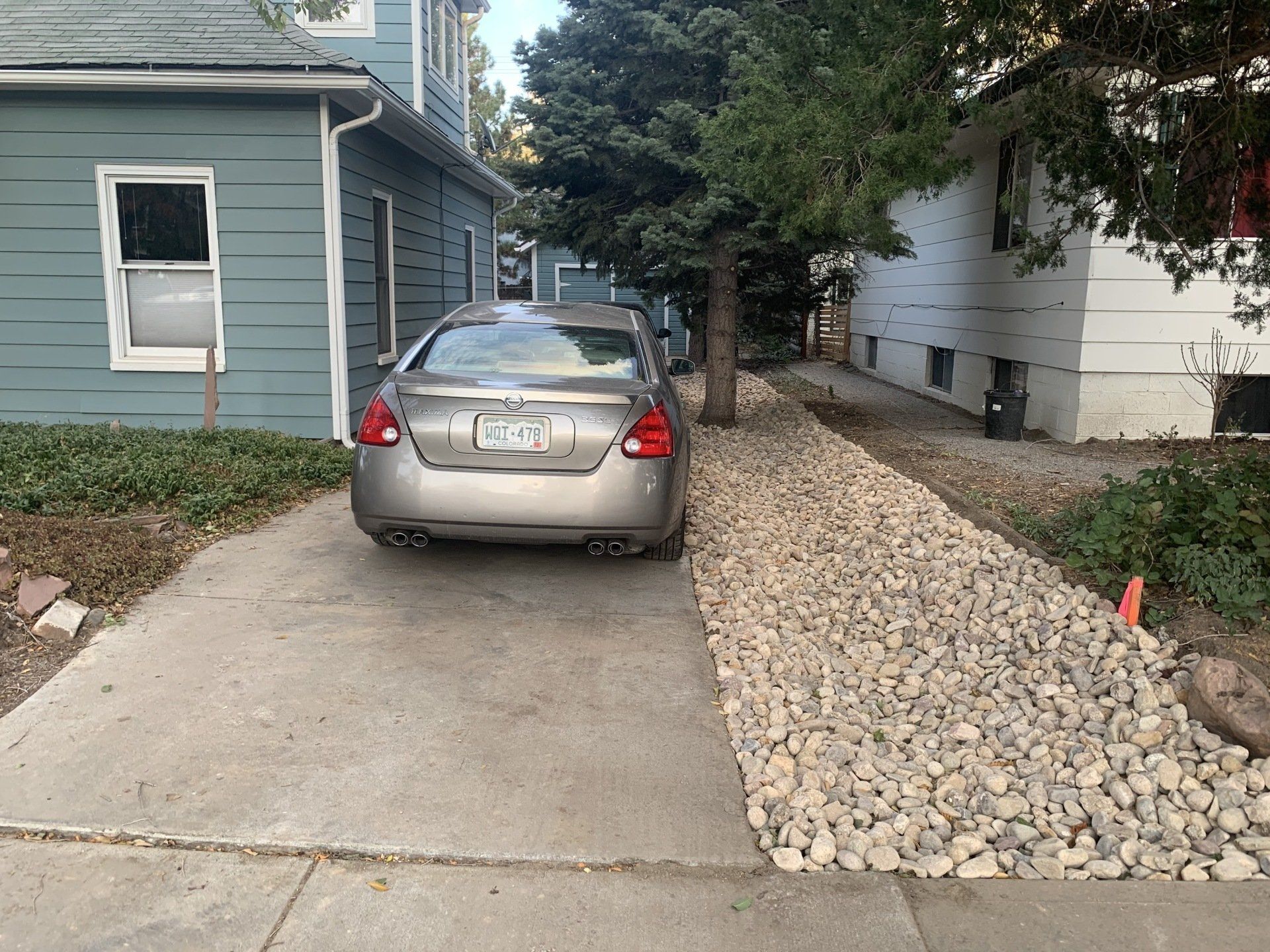 Car parked in a driveway between two houses, one blue and one white, with a rock garden alongside.