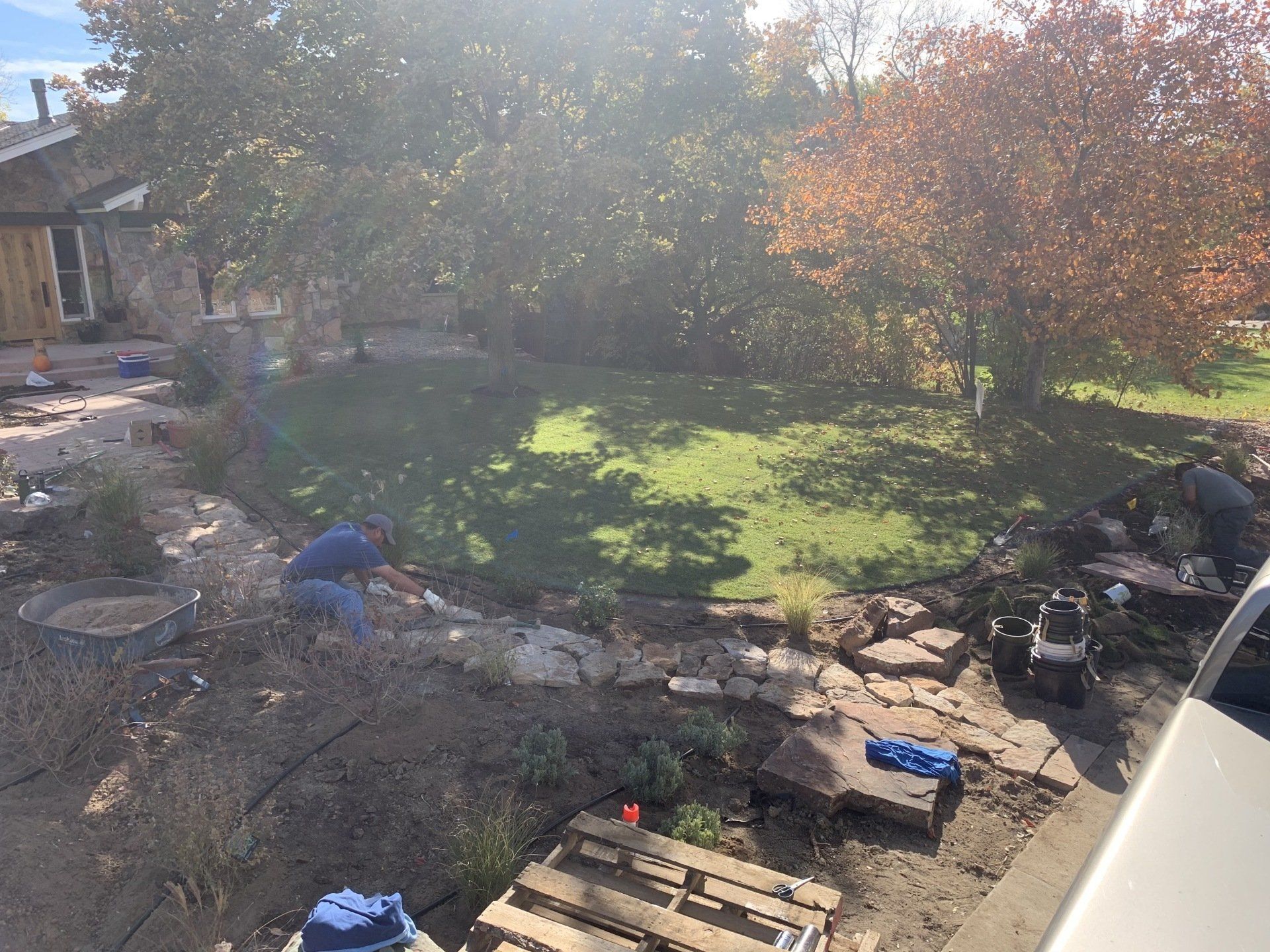 People working in a backyard with a lawn and trees; it appears to be fall.