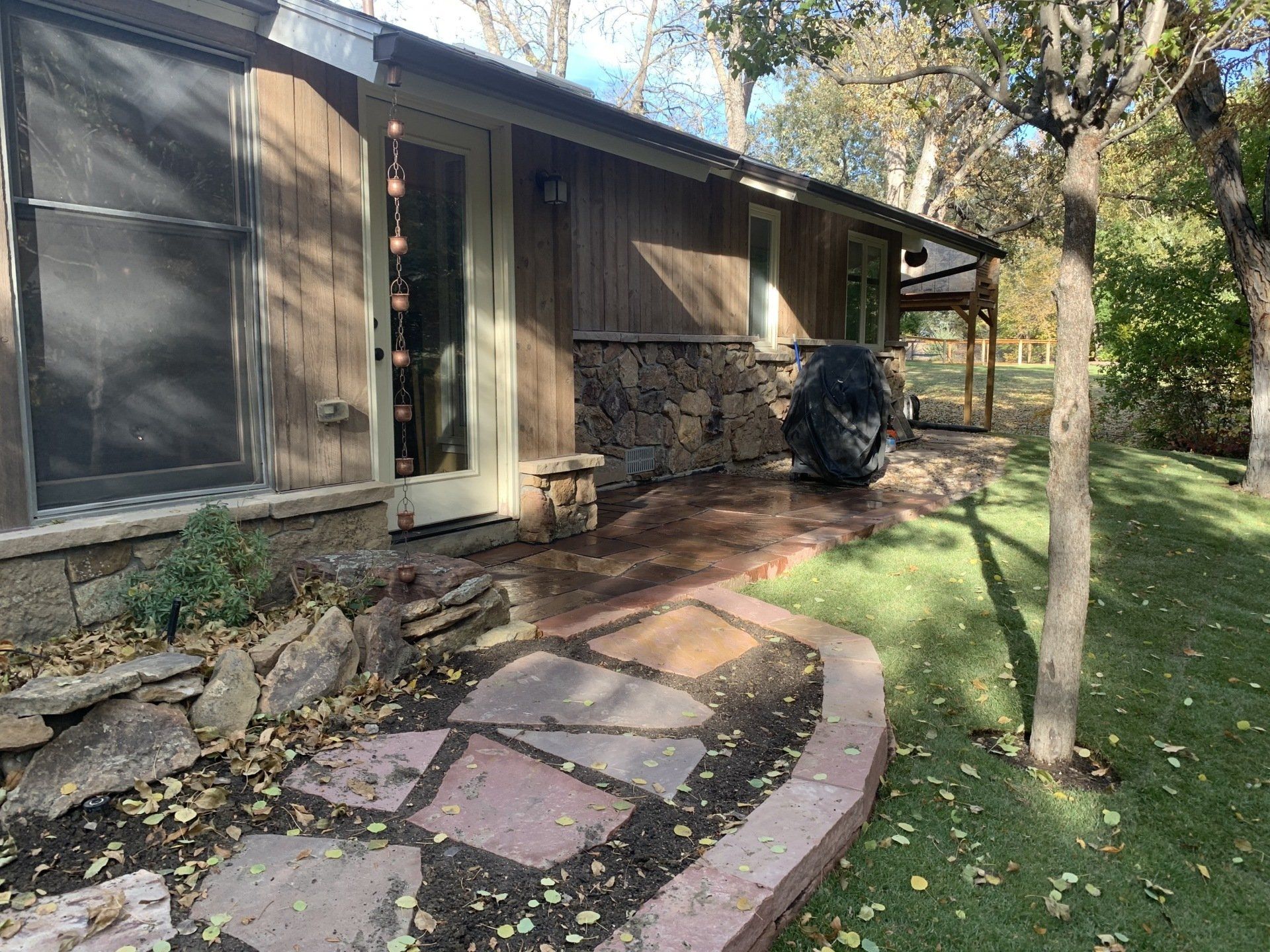 House exterior with flagstone patio, lawn, and trees. Brown siding and stone facade.