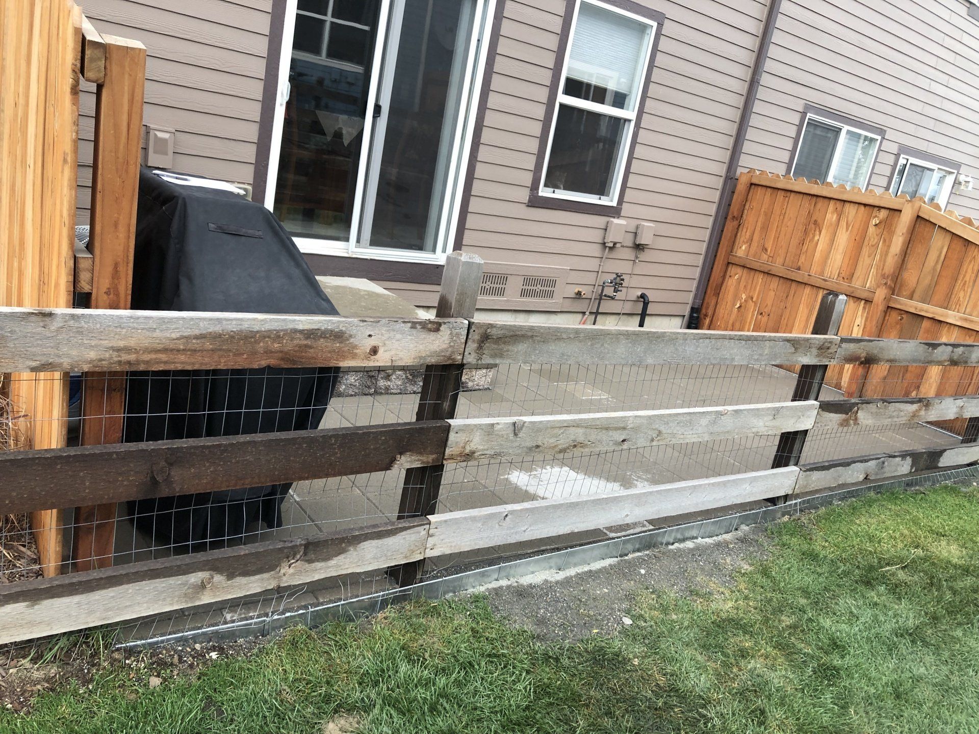Backyard with a wooden fence, grill, grass, and a house with a sliding glass door and windows.