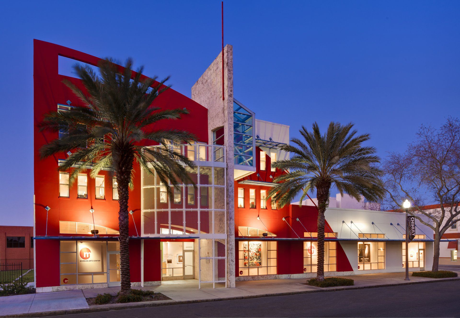 Red and white art gallery with palm trees and evening lighting.
