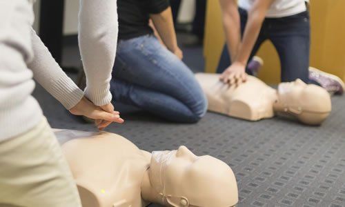 Personas practicando RCP en maniquíes. En interiores, en el suelo. Manos sobre el pecho, practicando compresiones.