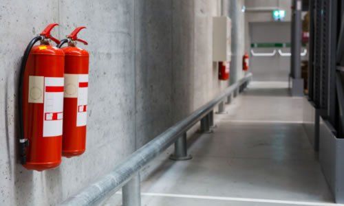 Dos extintores rojos montados en una pared de hormigón en un pasillo industrial.