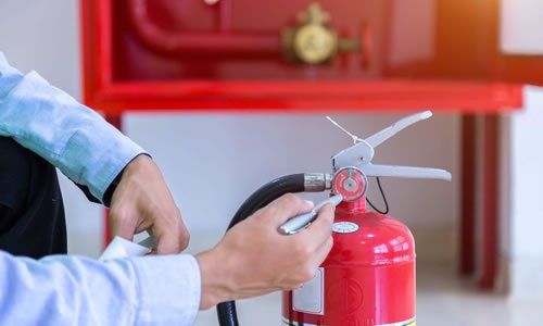 Persona inspeccionando un extintor rojo cerca de un armario rojo para mangueras contra incendios.