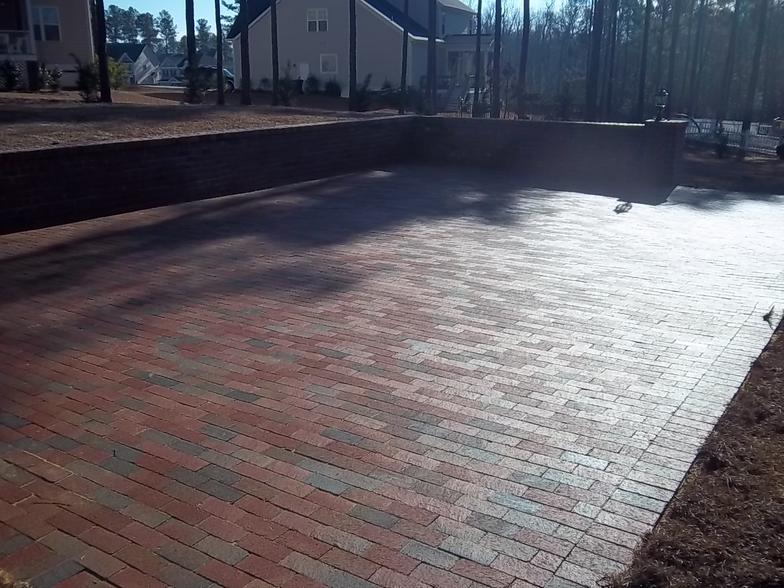 A brick walkway in front of a house with trees in the background