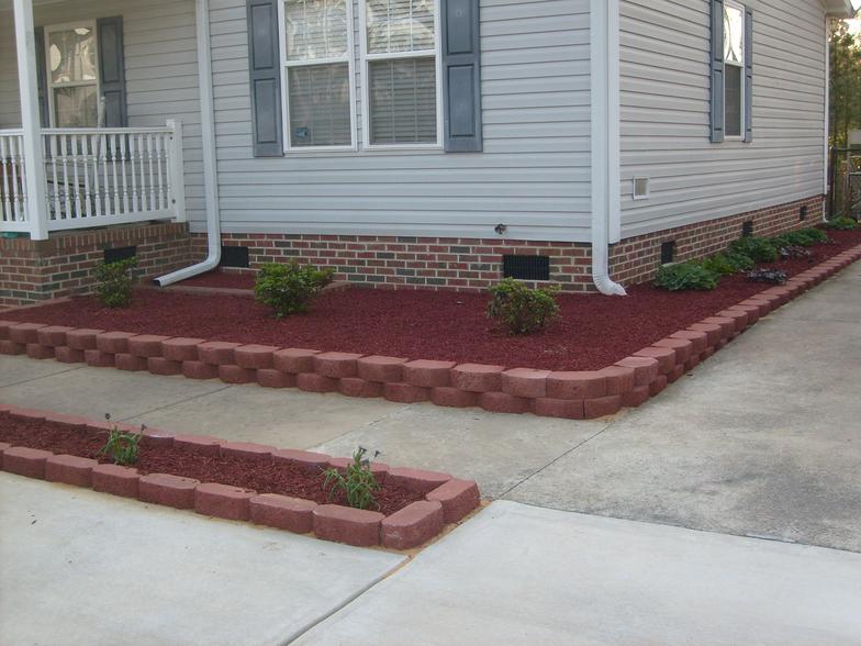 A white house with a brick foundation and red mulch in front of it