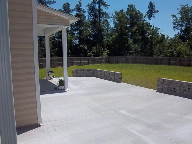 A concrete driveway leading to a house with a fence in the background.