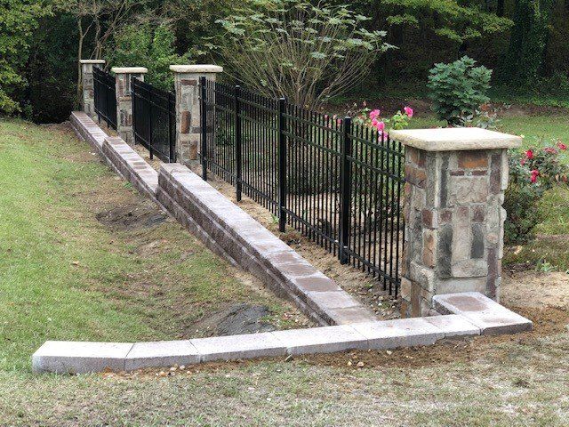 A fence with stone pillars and a metal fence in a yard.