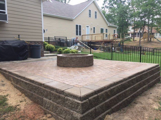 A patio with a fire pit in the middle of it and a house in the background.