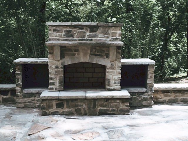 A stone fireplace is surrounded by trees on a patio