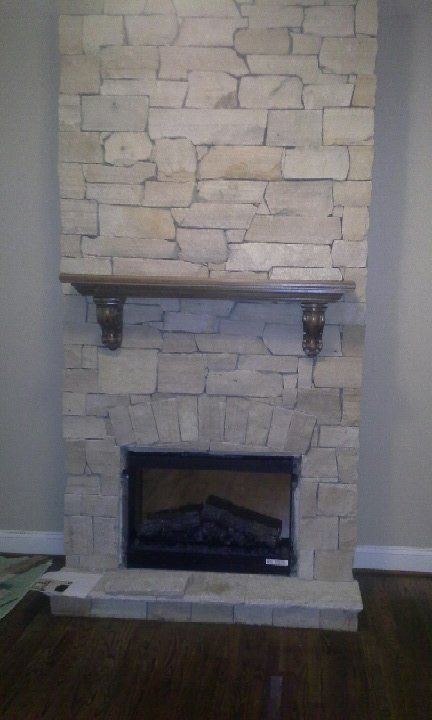 A stone fireplace with a shelf above it in a living room.