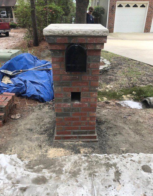 A brick mailbox is sitting in the dirt in front of a garage.