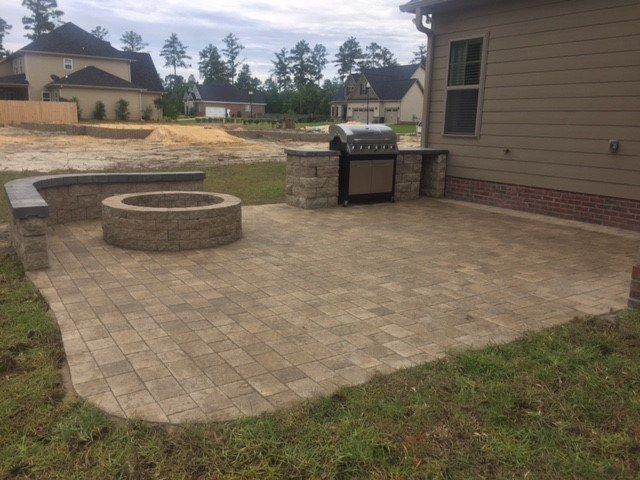 A patio with a fire pit and a grill in front of a house.