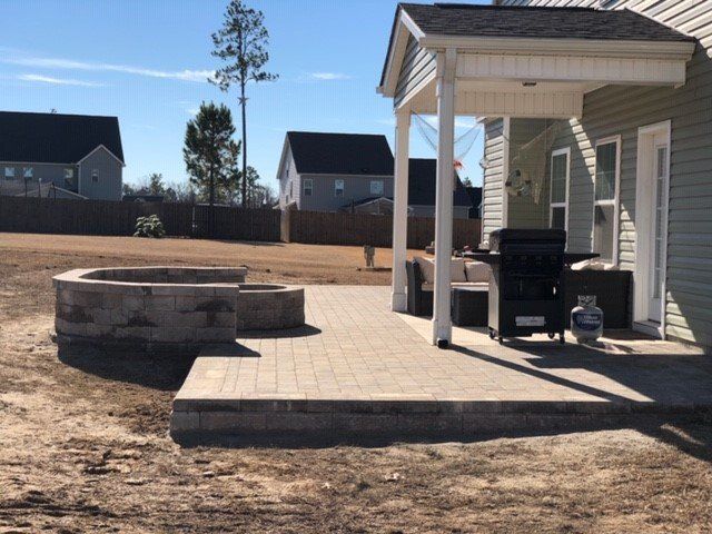 A patio with a grill and a fire pit in front of a house