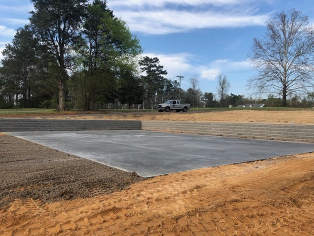A truck is driving down a dirt road next to a concrete slab.