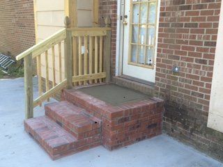 A brick porch with stairs and a wooden railing.