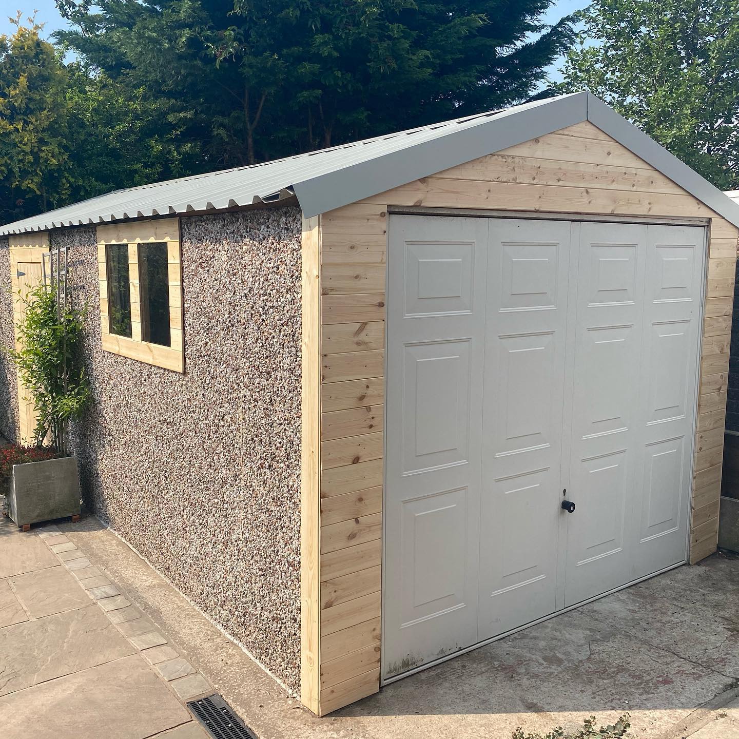 Light gray garage sheet roof with shot of pebbled-dash facade and timber personnel door