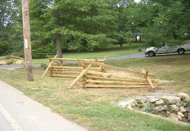 A white truck is parked on the side of the road next to a wooden fence.