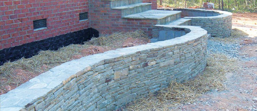A stone wall is being built in front of a brick building.