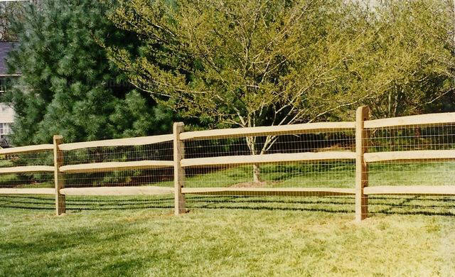 A wooden fence surrounds a lush green field with trees in the background.