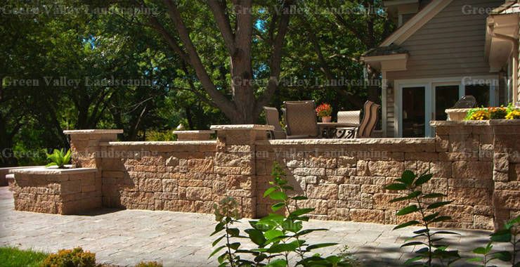 A stone wall surrounds a patio area in front of a house.