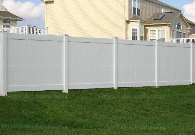 A white fence surrounds a lush green yard in front of a house
