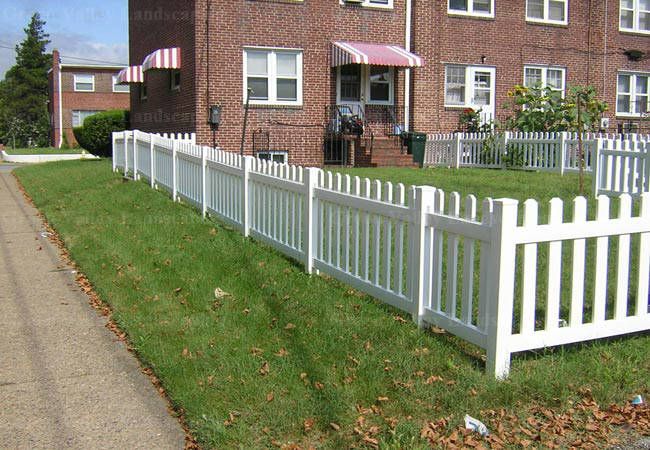 A white picket fence is in front of a brick building