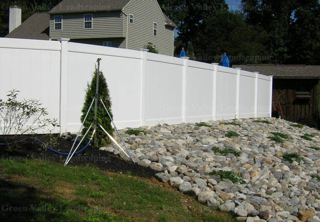 A white fence surrounds a rocky area in front of a house