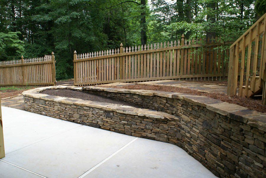 A stone wall with a wooden fence in the background