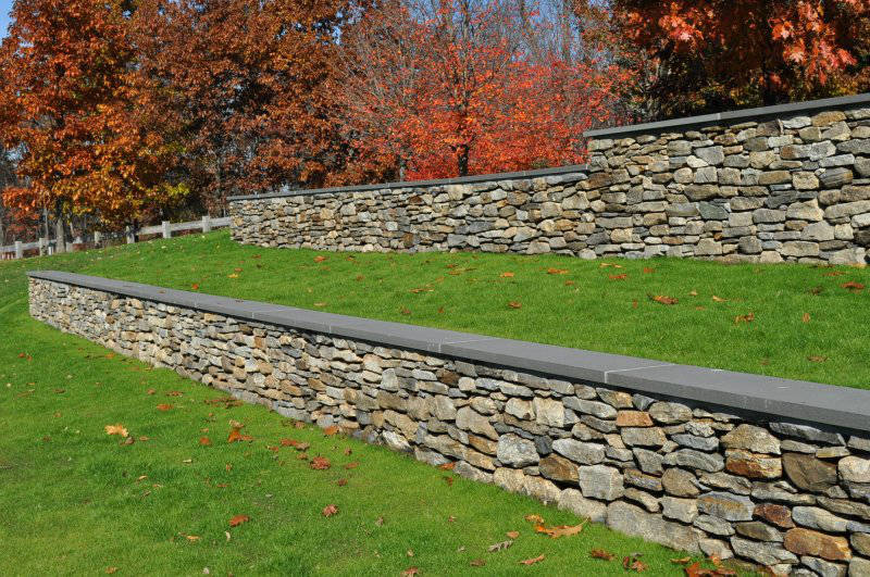A stone wall surrounds a lush green field with trees in the background.