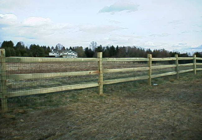 A wooden fence surrounds a field with a house in the background.