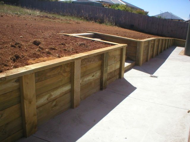 A concrete walkway with a wooden retaining wall in the background
