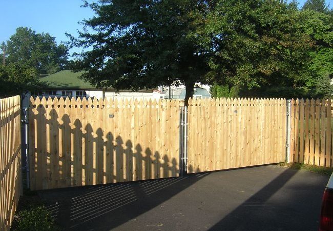 A wooden fence surrounds a driveway with trees in the background