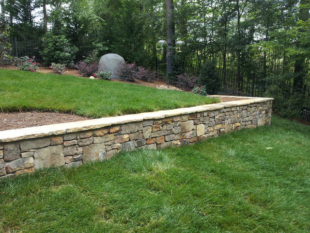 There is a stone wall in the middle of a lush green field.