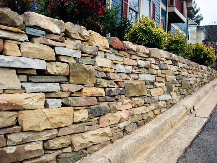 A stone wall along the side of a road next to a house.
