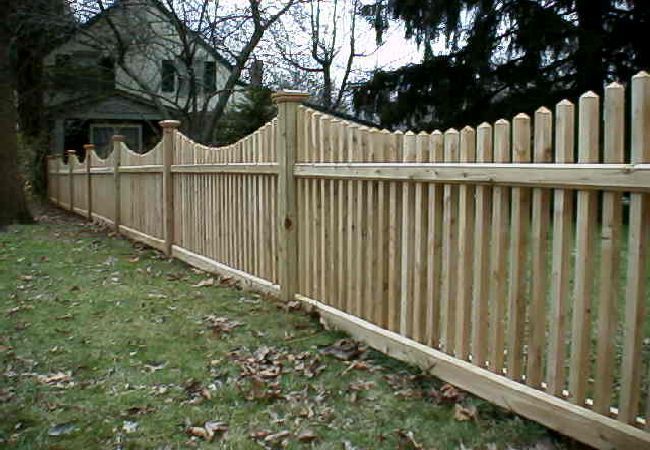A wooden picket fence surrounds a lush green yard in front of a house.