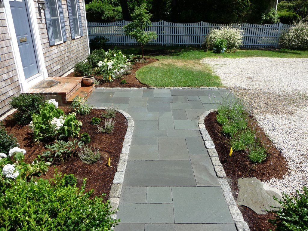 A stone walkway leading to a house with a white picket fence