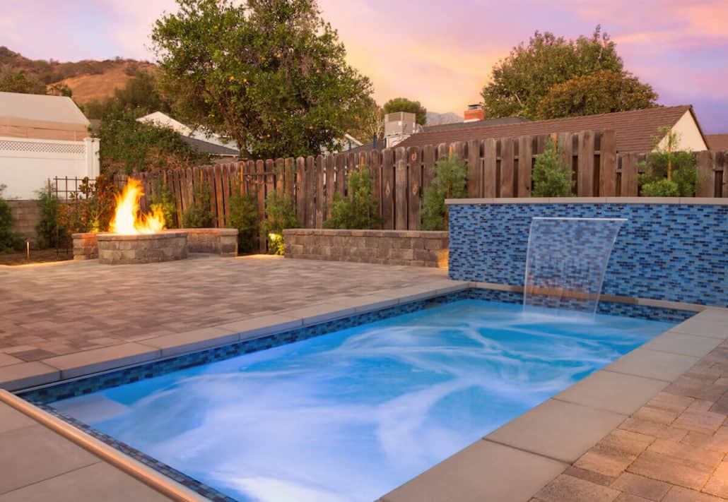 A swimming pool with a waterfall and a fire pit in the backyard.