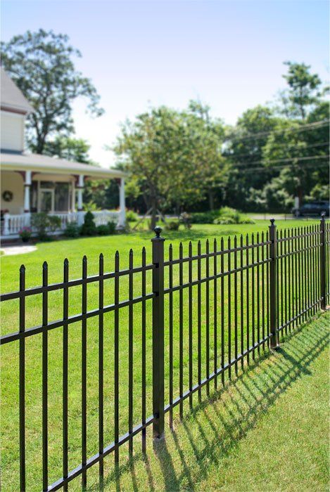 A wrought iron fence surrounds a lush green yard in front of a house.