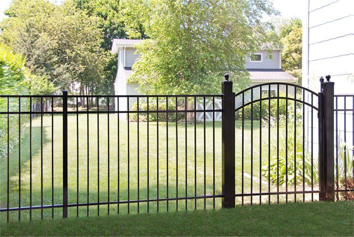 A black metal fence surrounds a lush green yard in front of a house.