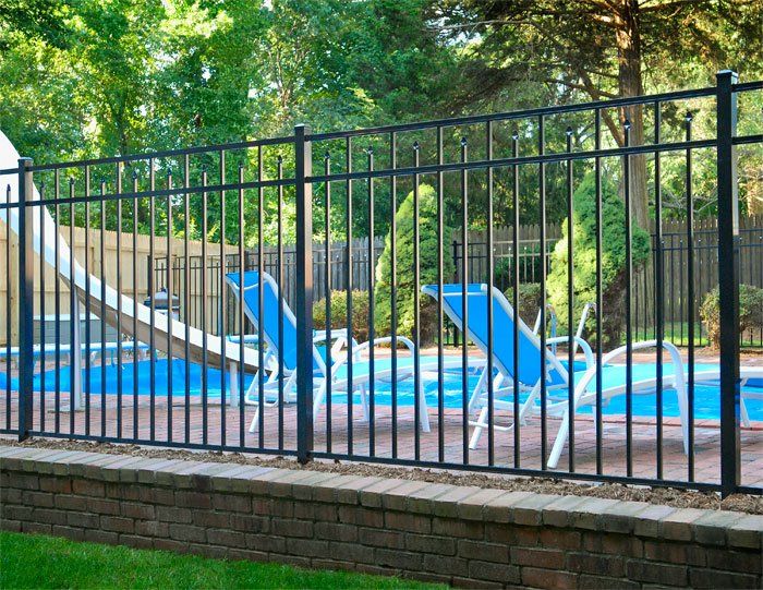 A black fence surrounds a swimming pool with chairs and a slide.