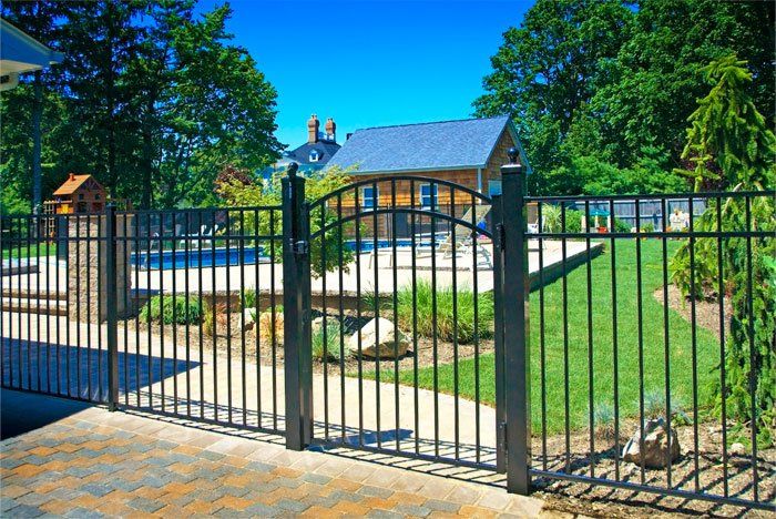 A wrought iron gate leading to a house with a pool in the background.
