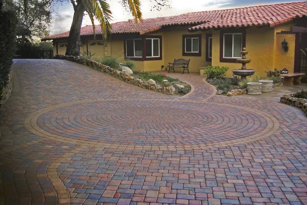 A brick driveway leading to a house with a red tile roof