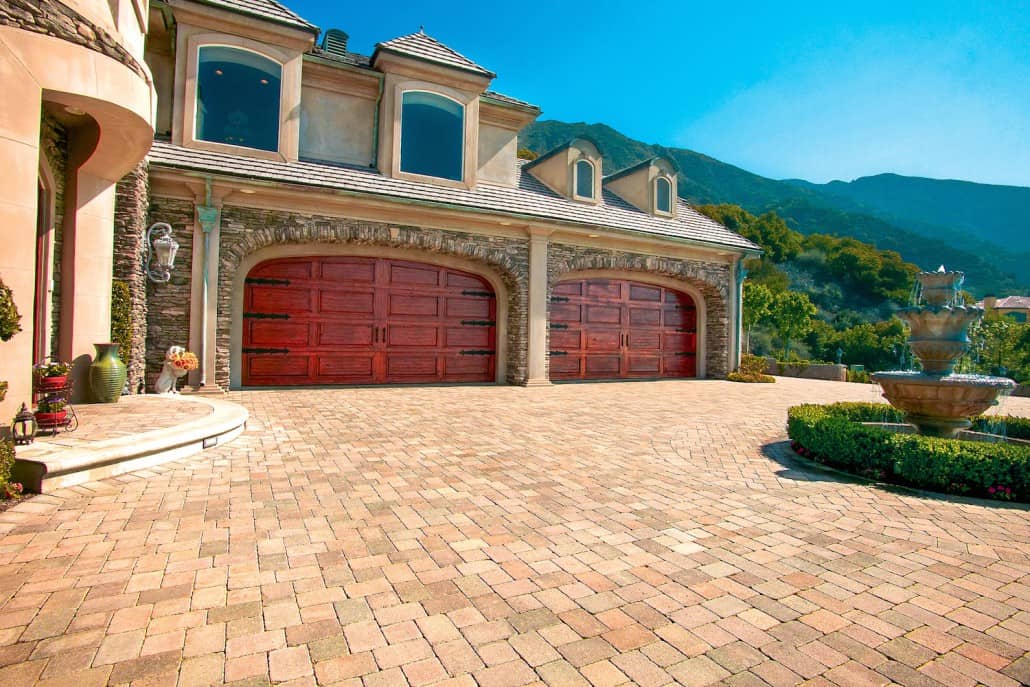 A large house with two red garage doors and a brick driveway.