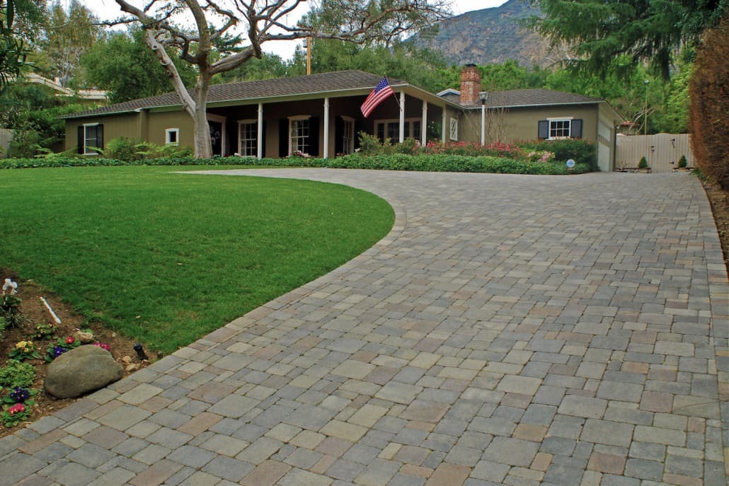 A brick driveway leading to a house with a lush green lawn.