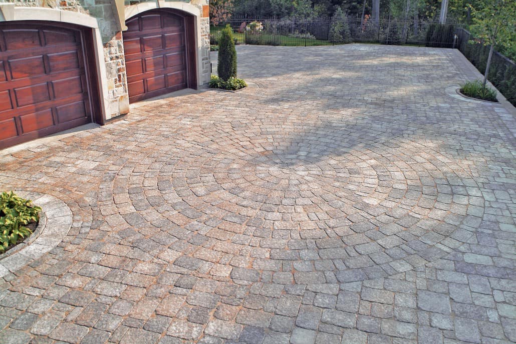 A brick driveway leading to a garage with two garage doors.