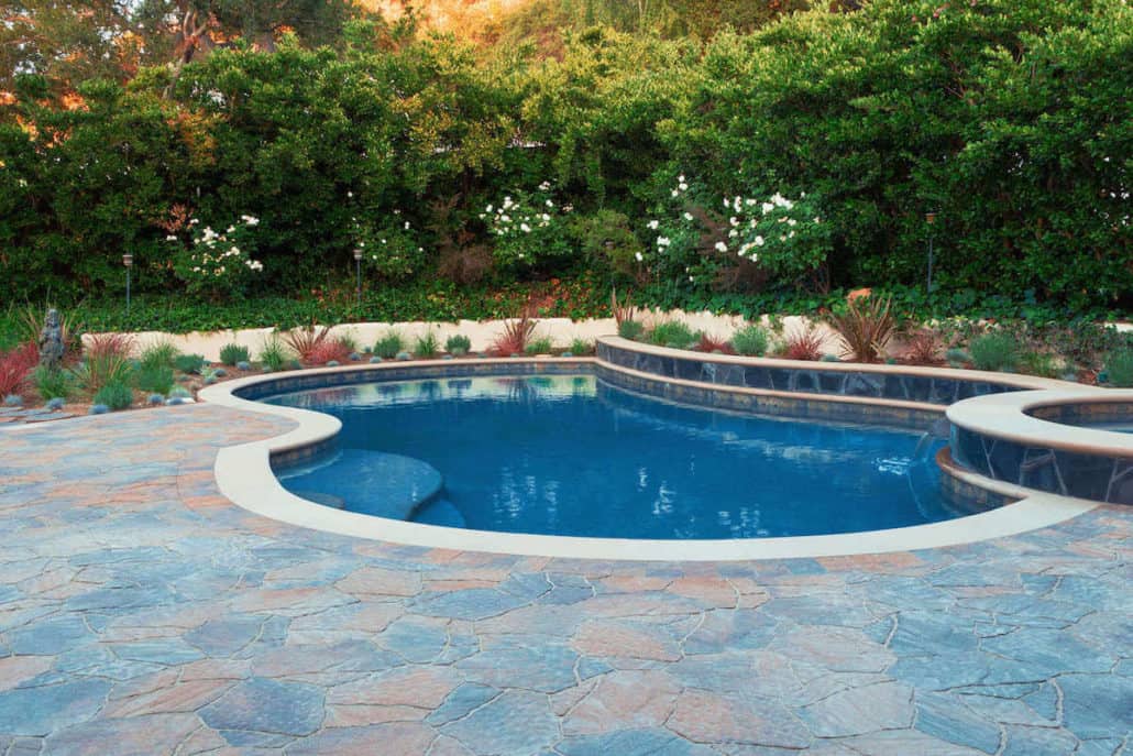 A large swimming pool is surrounded by trees and a patio.