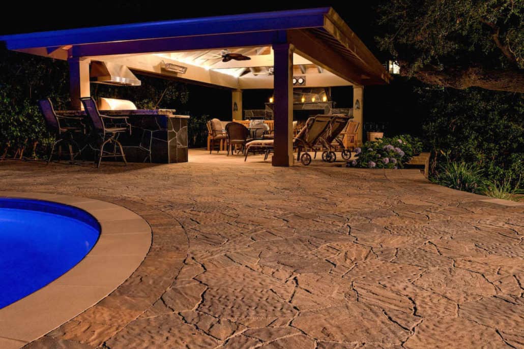 A patio with a pool and a gazebo at night.