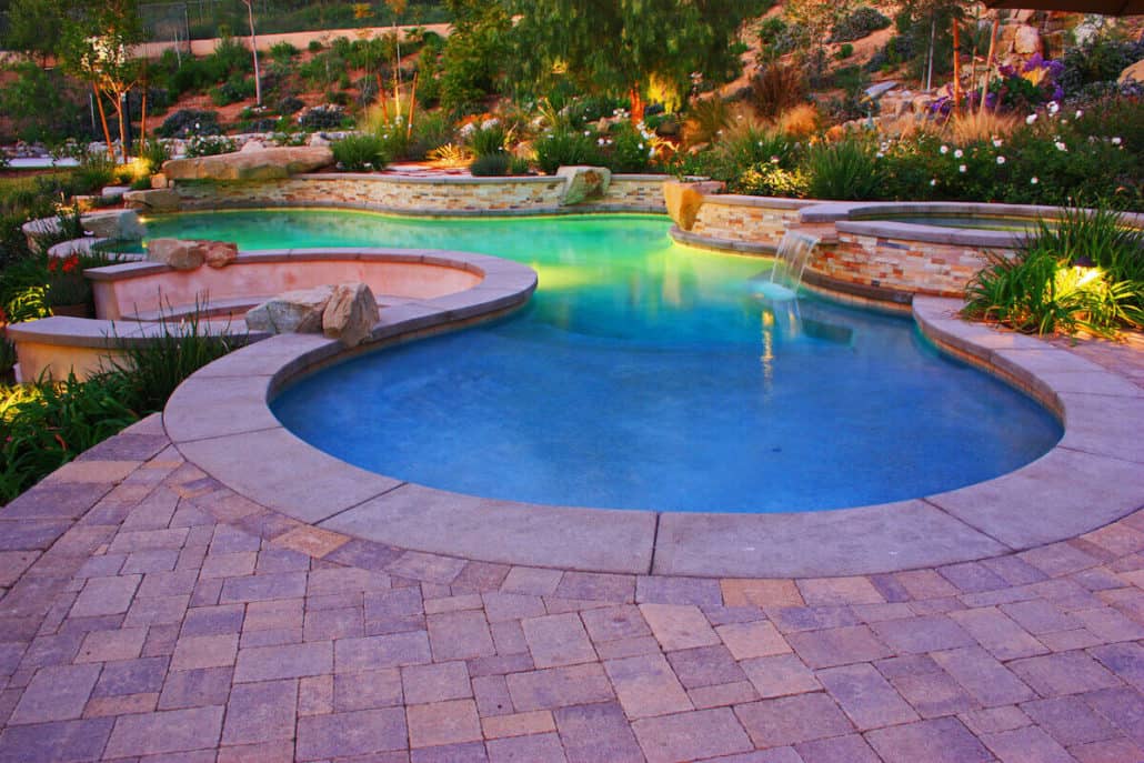 A large swimming pool is surrounded by a brick patio.